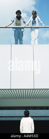Young people standing on balcony looking down at young man Stock Photo