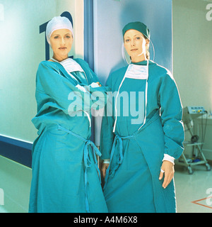 Two female doctors in operating gowns, leaning against doorframe Stock Photo