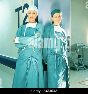 Two female doctors in operating gowns, leaning against doorframe Stock Photo