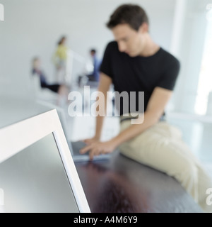 Man sitting on edge of desk in office Stock Photo