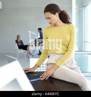 Woman sitting on edge of desk in office Stock Photo