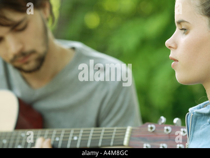 Young woman listening to young man playing guitar Stock Photo