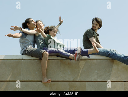 Young people sitting on top of wall with arms out Stock Photo