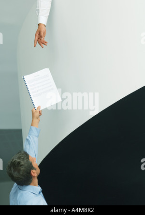 Man holding up document for second person reaching down Stock Photo