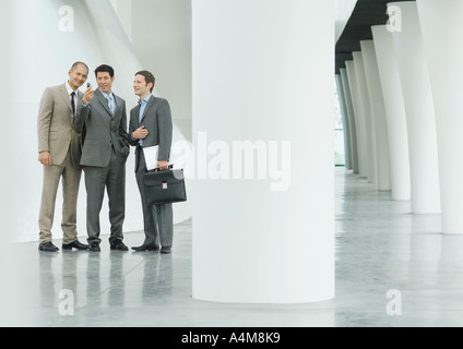 Three businessmen looking at cell phone in lobby Stock Photo