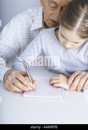Grandfather helping granddaughter write in notebook Stock Photo