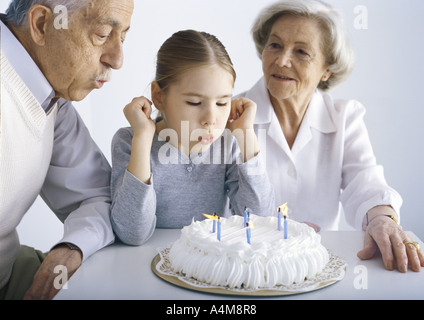 Girl sitting with grandparents, blowing out candles on cake Stock Photo