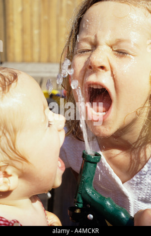 Two young girls drinking from garden hose Stock Photo