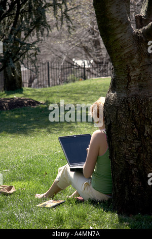Woman sitting on grass leaning against tree trunk using laptop computer outdoors at Georgetown University campus Washington DC Stock Photo
