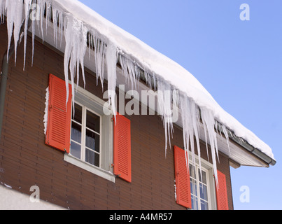 Row of lovely long icicles hang from gutter and roof of house with red shutters in Engelberg in central Switzerland Stock Photo