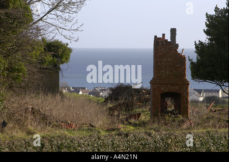 ruin of an old chimney stack in a ruined ancient house overlooking modern housing and sea at Carnlough county Antrim Stock Photo