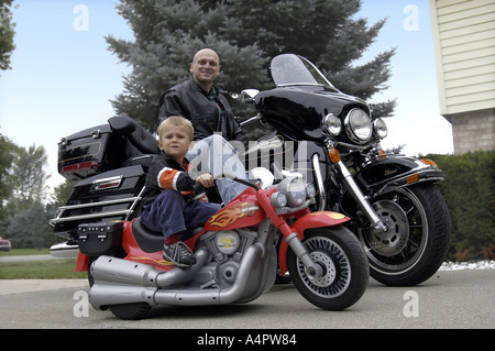 Bald Caucasion father leather jacket Harley Davidson FLHTC Electra Glide Classic Background Son on Fisher Price Motorcycle Stock Photo