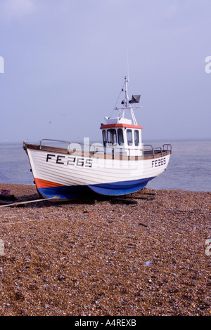 Small red, white and blue fishing boat on the beach at Dungeness in Kent  vertical Stock Photo