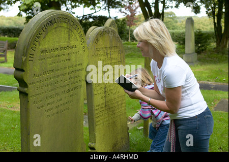 lady looking at details on a gravestone with her daughters Stock Photo