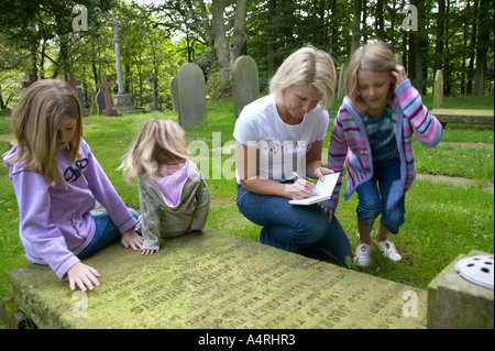 lady looking at details on a gravestone with her daughters Stock Photo