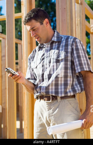 Young male contractor at construction site using mobile phone. Stock Photo