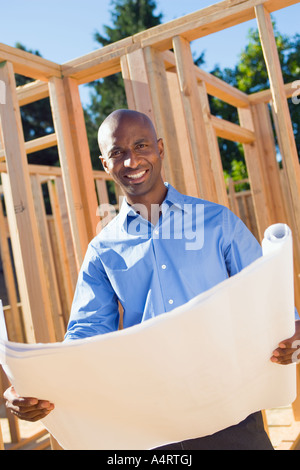 Portrait of young male professional at building site with plans.  skilled skillful skills smile smiling structure structures sun Stock Photo