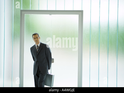 Businessman standing in front of door, holding briefcase behind back Stock Photo