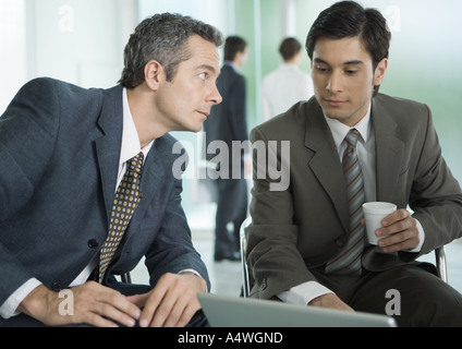 Two businessmen sitting around laptop, one with coffee cup Stock Photo