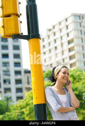 Young woman leaning against traffic-light post, talking on cell phone Stock Photo