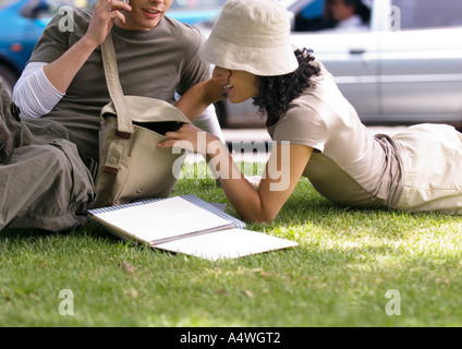 Young couple relaxing on grass, woman reaching into man's bag Stock Photo