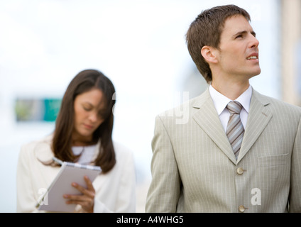 Businessman looking up while female assistant takes notes in background Stock Photo