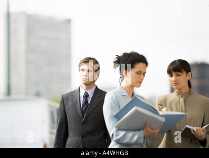Two businesswomen discussing file, businessman passing by in background Stock Photo