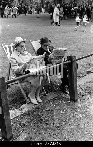 Older couple reading newspapers St James Park central London sitting in deckchairs deck chairs England 1971 1970s UK HOMER SYKES Stock Photo