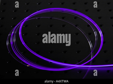 A cladding-pumped doped optical fiber glowing on an optical table Stock Photo