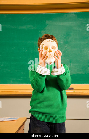 Boy holding skull over face in classroom Stock Photo