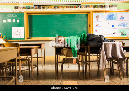 Boy sleeping on desks in classroom Stock Photo
