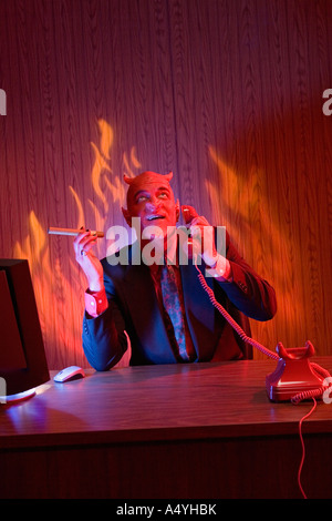 Businessman dressed as devil talking on telephone Stock Photo
