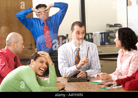 Businessman making faces through glass wall at co-workers Stock Photo