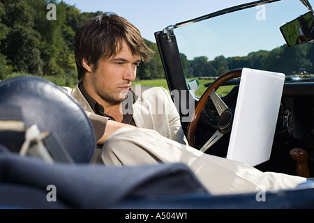 Man in convertible using laptop Stock Photo