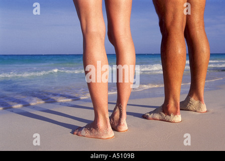 Man and womans legs seen standing on beach along shoreline Caribbean Stock Photo