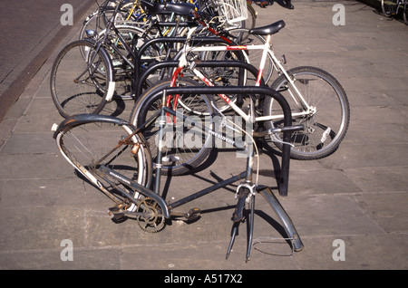 Cambridge university town line of parked cycles with one inscribed President minus one wheel and vandalised Stock Photo