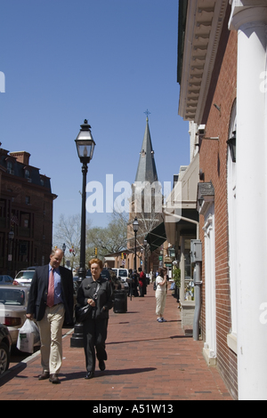 Man and woman walk along brick sidewalk on Main Street in Annapolis Maryland with St Annes Episcopal Church in the distance Stock Photo