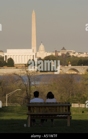 Couple sitting on bench with Lincoln Memorial Washington Monument and Capitol Building in distance from Arlington Virginia USA Stock Photo