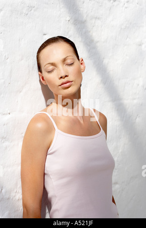 A young woman leaning against a wall eyes closed Stock Photo