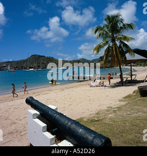 People on beach and enjoying boating activities in English Harbour old mounted cannon in foreground Antigua The Caribbean Stock Photo