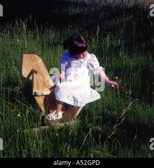 girl in white dress sitting on a horselike wooden rocking chair.  Photo by Willy Matheisl Stock Photo