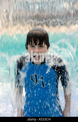 Young boy smiling in water fall waterfall cooling off at playground in summer.  Properties of water.  Water is a powerful evapor Stock Photo