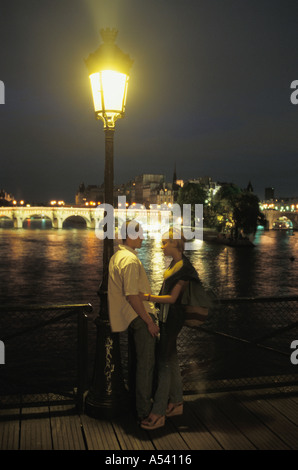 Young couple on Pont des Arts with River Seine and Pont Neuf behind at night Stock Photo