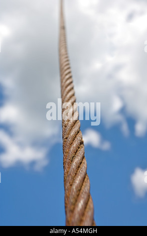 Rusty steel rope cable up to heavens against blue sky and clouds Stock Photo