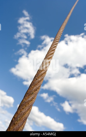 Rusty steel rope cable up to heavens against blue sky and white clouds Stock Photo