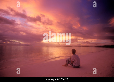 Woman sitting on beach watching colourful sunset in Maluku Indonesia Model Released Photo Stock Photo