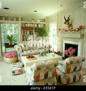 Pale Ikat-style patterned sofas and armchairs beside fireplace in white eighties living room with baskets of pink hydrangeas Stock Photo