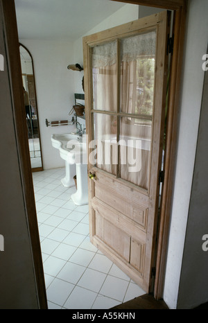 Open half-glazed wooden door to dining room with white tiled floor Stock Photo