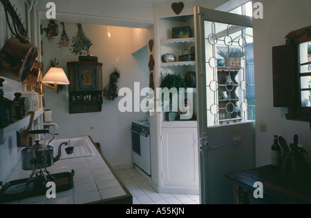 White kitchen with wall-light above tiled worktop and open half-glazed door Stock Photo