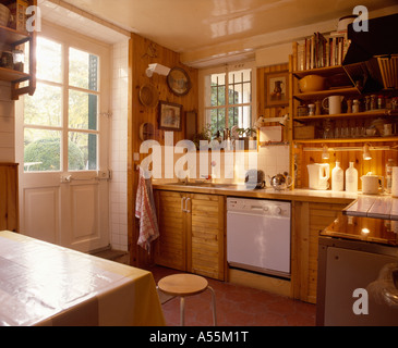 Country kitchen with dishwasher in wooden units below underlit shelves and half-glazed back door Stock Photo